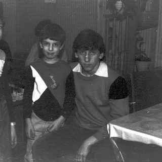 Three young boys posing indoors, wearing sweaters and pants.