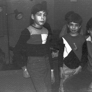 Three young boys posing indoors, wearing sweaters and pants.