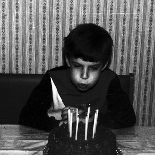 Black and white photo of a boy blowing out candles.