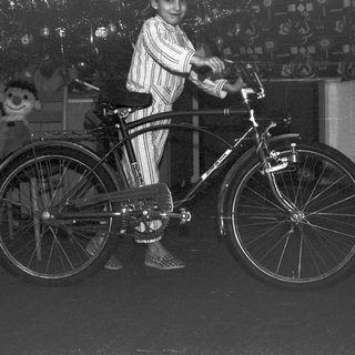 Boy in pajamas poses with a vintage bicycle indoors.