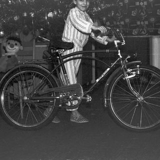 Boy in pajamas poses with a vintage bicycle indoors.