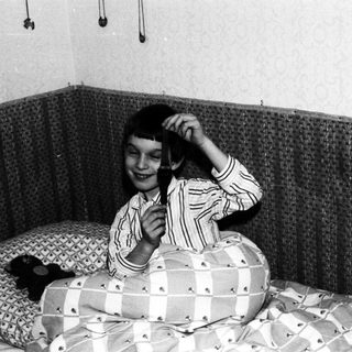 Here's a brief summary of the image: Child in striped pajamas sits on a bed, holding something.