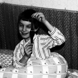 Here's a brief summary of the image: Child in striped pajamas sits on a bed, holding something.