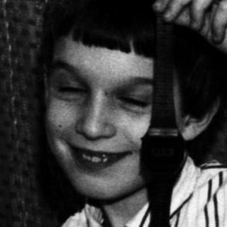 Here's a brief summary of the image: Child in striped pajamas sits on a bed, holding something.