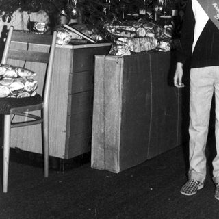 Boy stands near a Christmas tree and wrapped gifts.