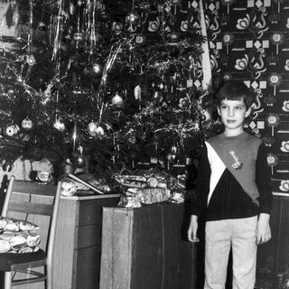 Boy stands near a Christmas tree and wrapped gifts.