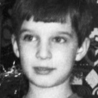 Boy stands near a Christmas tree and wrapped gifts.