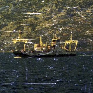 A ship sits in the water, facing a mountainous coastline.