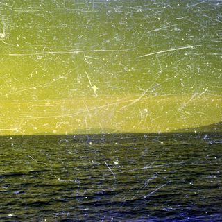 Here's a brief summary of the image: Dark water meets a yellow sky with distant land.