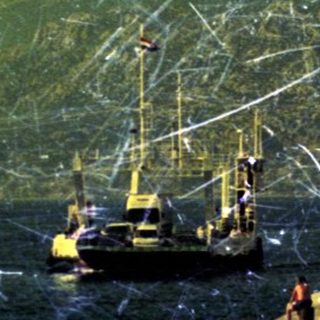 Boat and workers near a coastline with mountains.