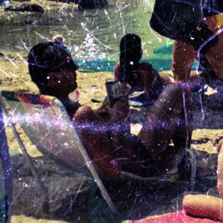 Children play on a sandy beach under a tree.