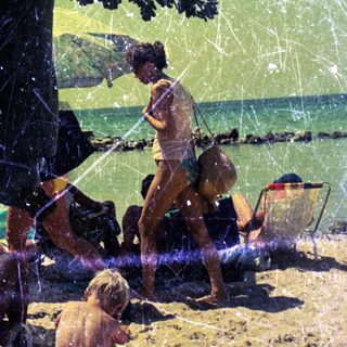 Children play on a sandy beach under a tree.