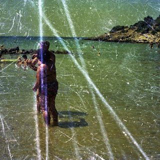 People swimming and wading in a shallow, sunny beach.