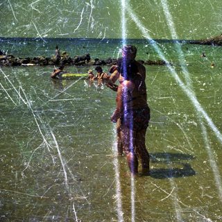People swimming and wading in a shallow, sunny beach.