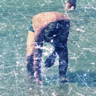 People swim in a clear, shallow, rocky beach.