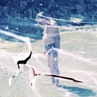 Here's a brief summary of the image: Person standing on a beach with foliage in the background.