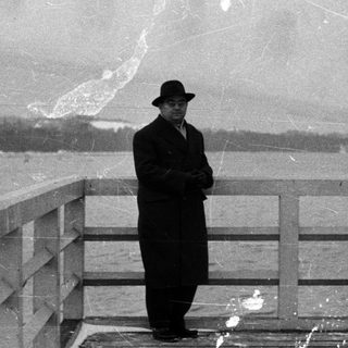 Man in coat stands on a pier overlooking water.