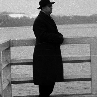 Man in hat stands overlooking water, looking away.