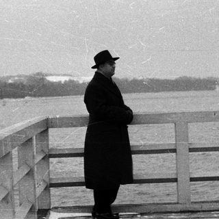 Man in hat stands overlooking water, looking away.