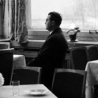 Man seated in a formally set, dimly lit restaurant.