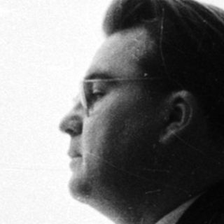 Man in suit stands looking out a window.