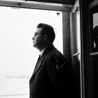 Man in suit stands looking out a window.