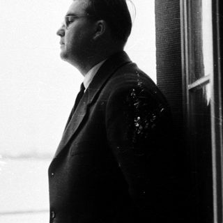 Man in suit stands looking out a window.