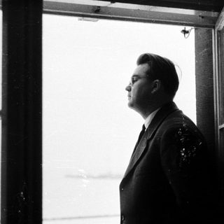 Man in suit stands looking out a window.