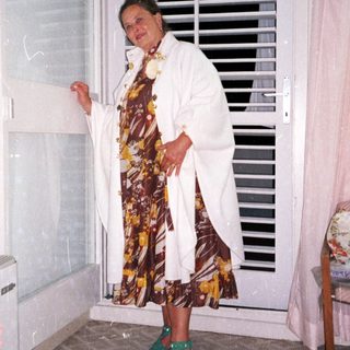 Woman stands near a window in a patterned dress.