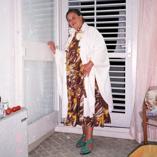 Woman stands near a window in a patterned dress.