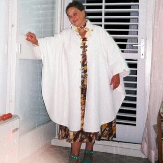 Woman in a robe stands near a window, smiling.