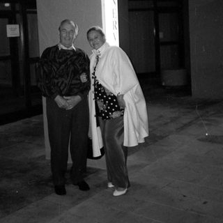 Here's a brief summary of the image: Couple stands near a building entrance at night.