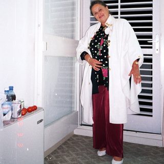 Woman stands near a door, wearing a robe and pants.
