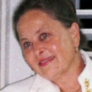 Woman in a white robe stands near a window.