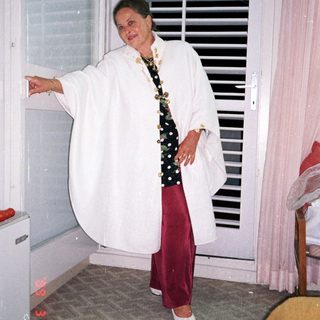 Woman in a white robe stands near a window.