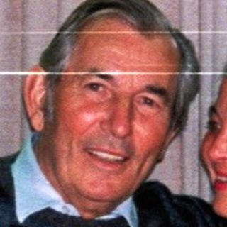 An elderly couple sits together at a table indoors.