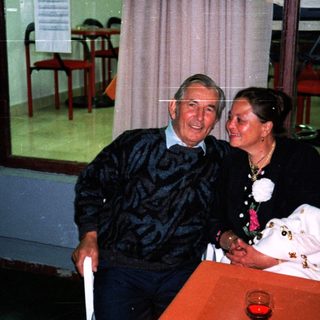 An elderly couple sits together at a table indoors.