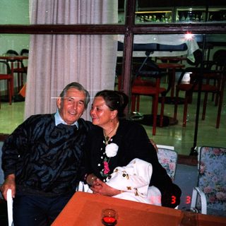 An elderly couple sits together at a table indoors.