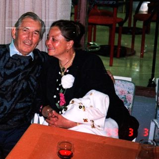 An elderly couple sits together at a table indoors.