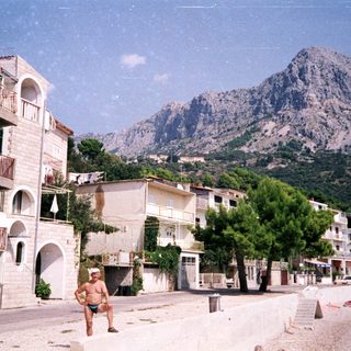 Coastal town with mountains, beach, and a man standing.