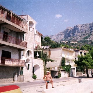 Coastal town with mountains, beach, and a man standing.