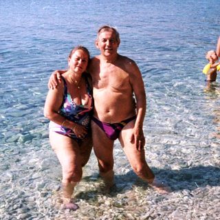 Couple and others stand in shallow, clear water near a beach.