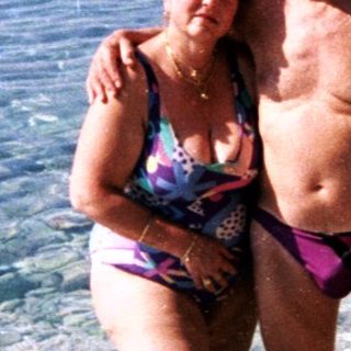 Couple and others stand in shallow, clear water near a beach.