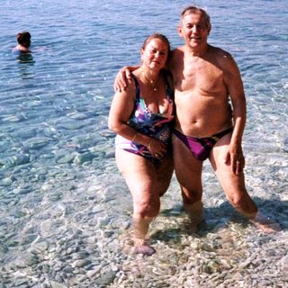 Couple and others stand in shallow, clear water near a beach.