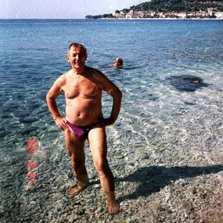 Man stands in shallow water with a beach and sea.
