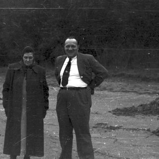 Three people stand outdoors, appearing to be in a rural setting.