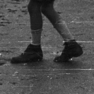 Boy walks along a riverbank holding a stick.