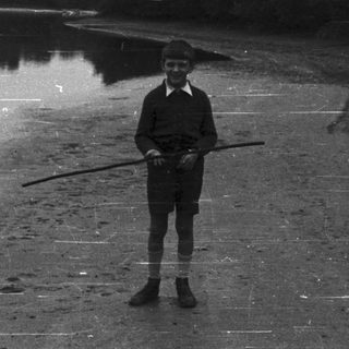 Boy standing on a beach holding a stick.