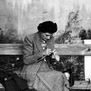 Boy sits beside a woman knitting on a bench.