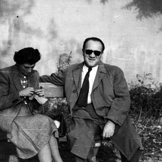 Couple seated on a bench, woman knitting, man reading.